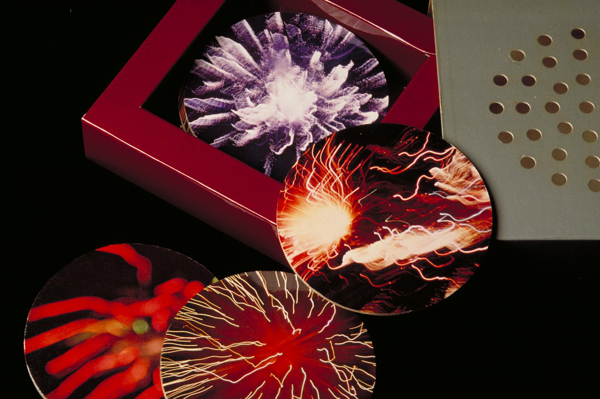 Colorful coasters with abstract, energetic patterns in red, white, and orange, displayed in and around a red box on a black surface.