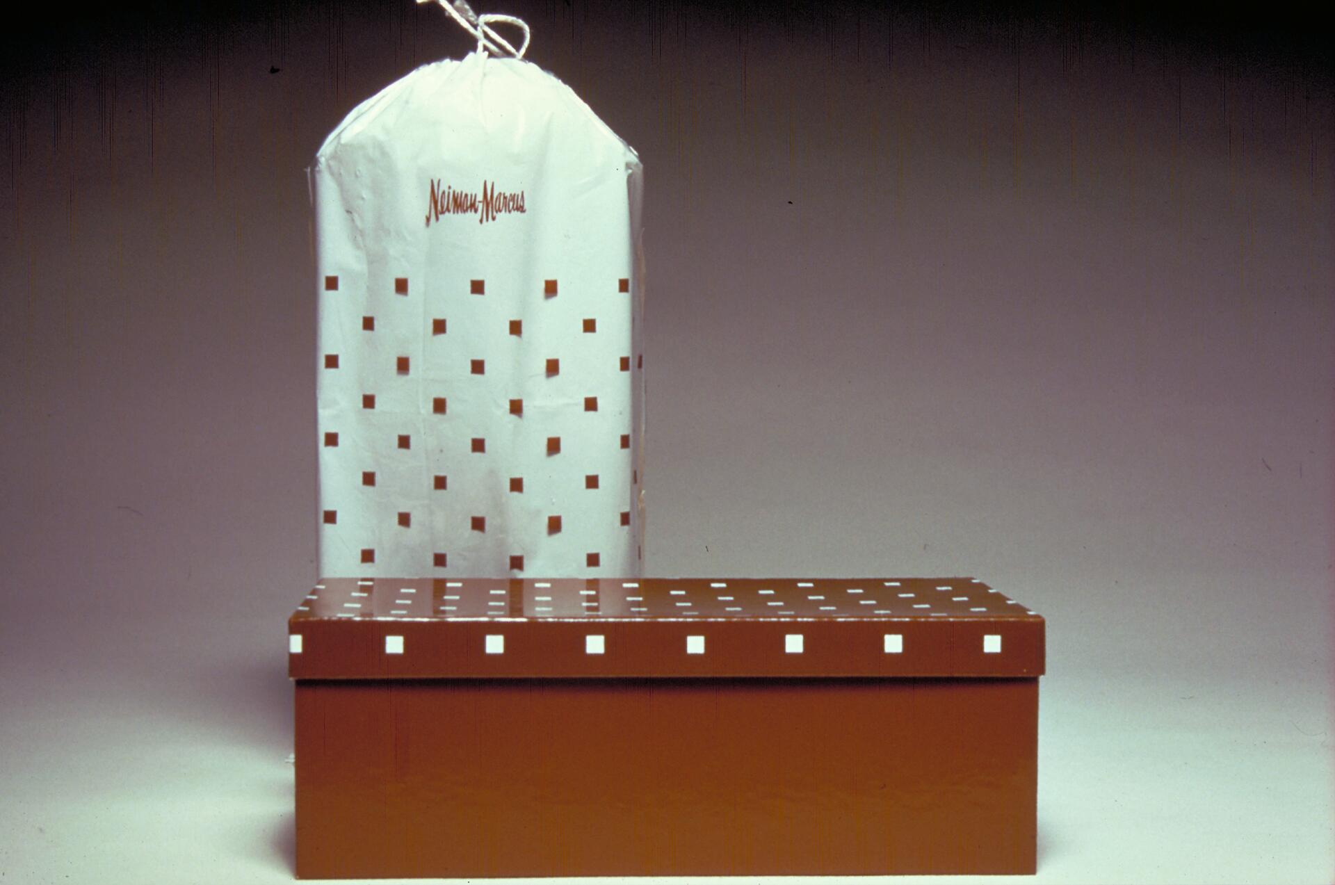 Brown gift box with a white lid featuring a red and white square pattern, set against a gray background. A matching white gift bag with red text and the same pattern stands behind the box.