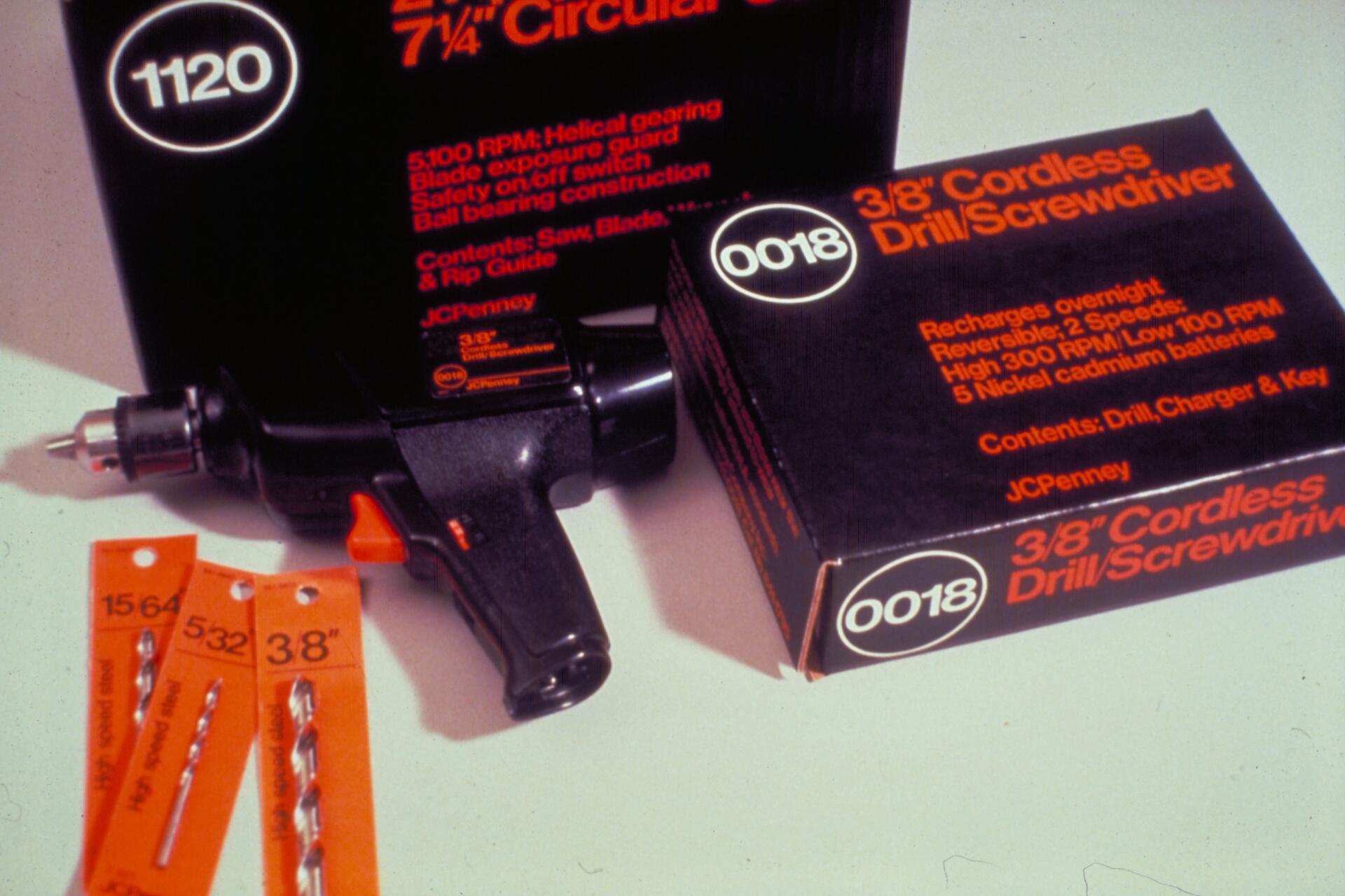 Cordless drill and screwdriver set with black and orange packaging, labeled JCPenney. Three metal drill bits in orange holders are placed nearby.
