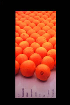 Rows of bright orange balls on a reflective surface with some text visible at the bottom edge.