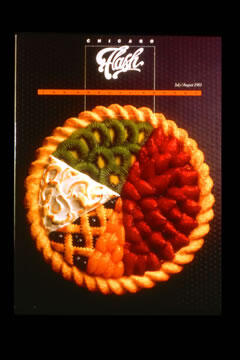 A colorful pie chart made of fruit slices, including kiwi, strawberries, mandarin oranges, and a lemon meringue section, against a dark background.