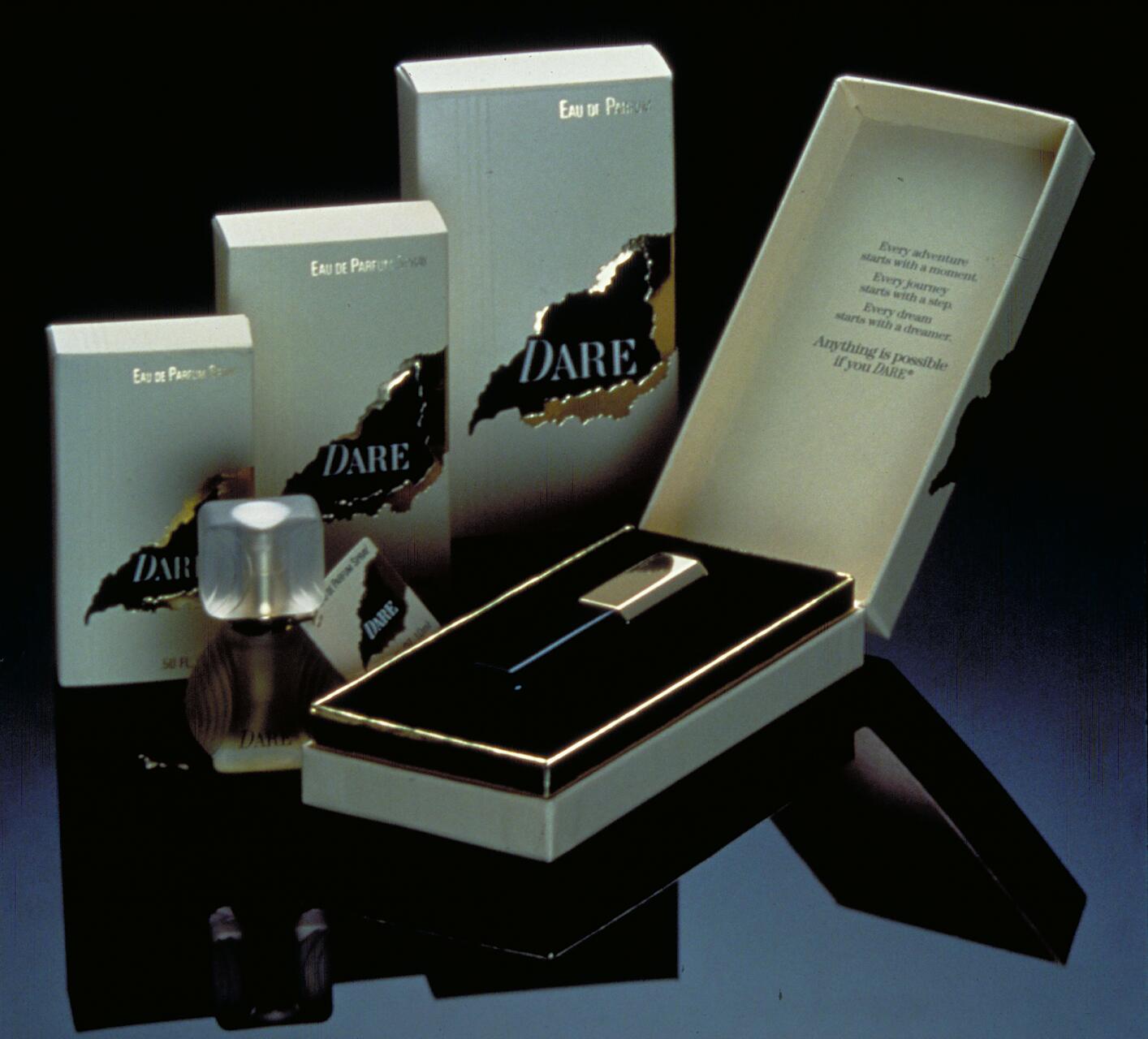 Perfume set with three DARE branded Eau de Parfum boxes, an opened gift box, and a small perfume bottle with a frosted cap, displayed on a reflective surface.