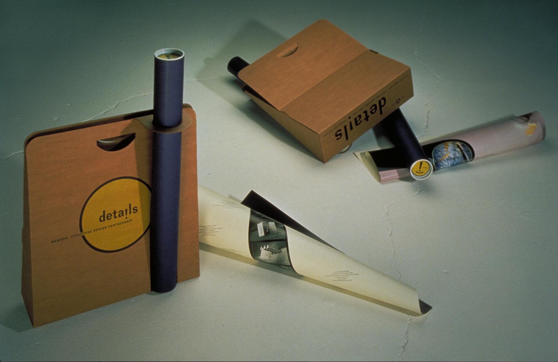 Brown paper bags and rolled posters on a light surface, each labeled "details," with a circular logo visible.