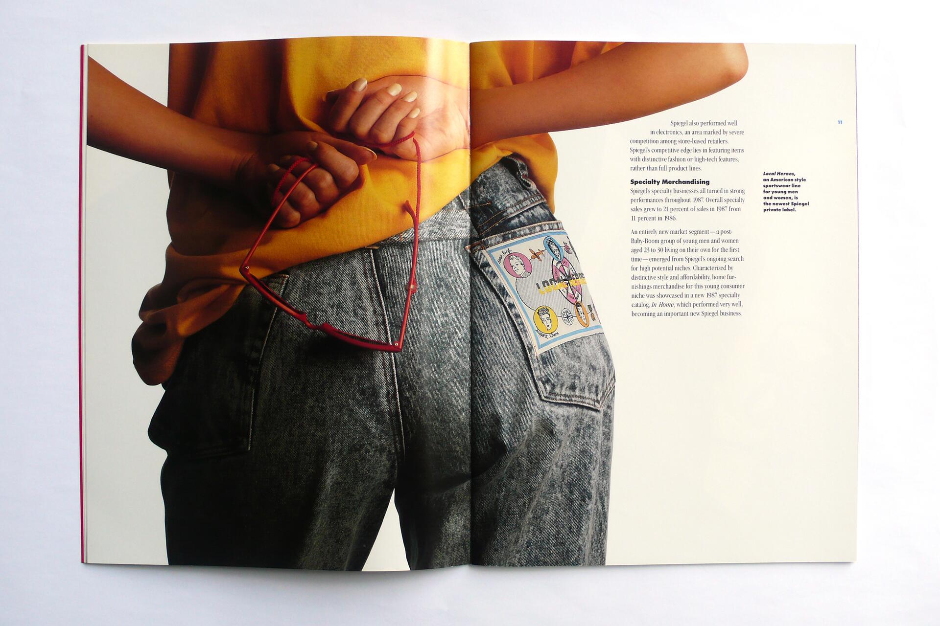 Person in a yellow shirt and light blue jeans holding red-framed glasses behind their back, with a colorful patch on the back pocket.