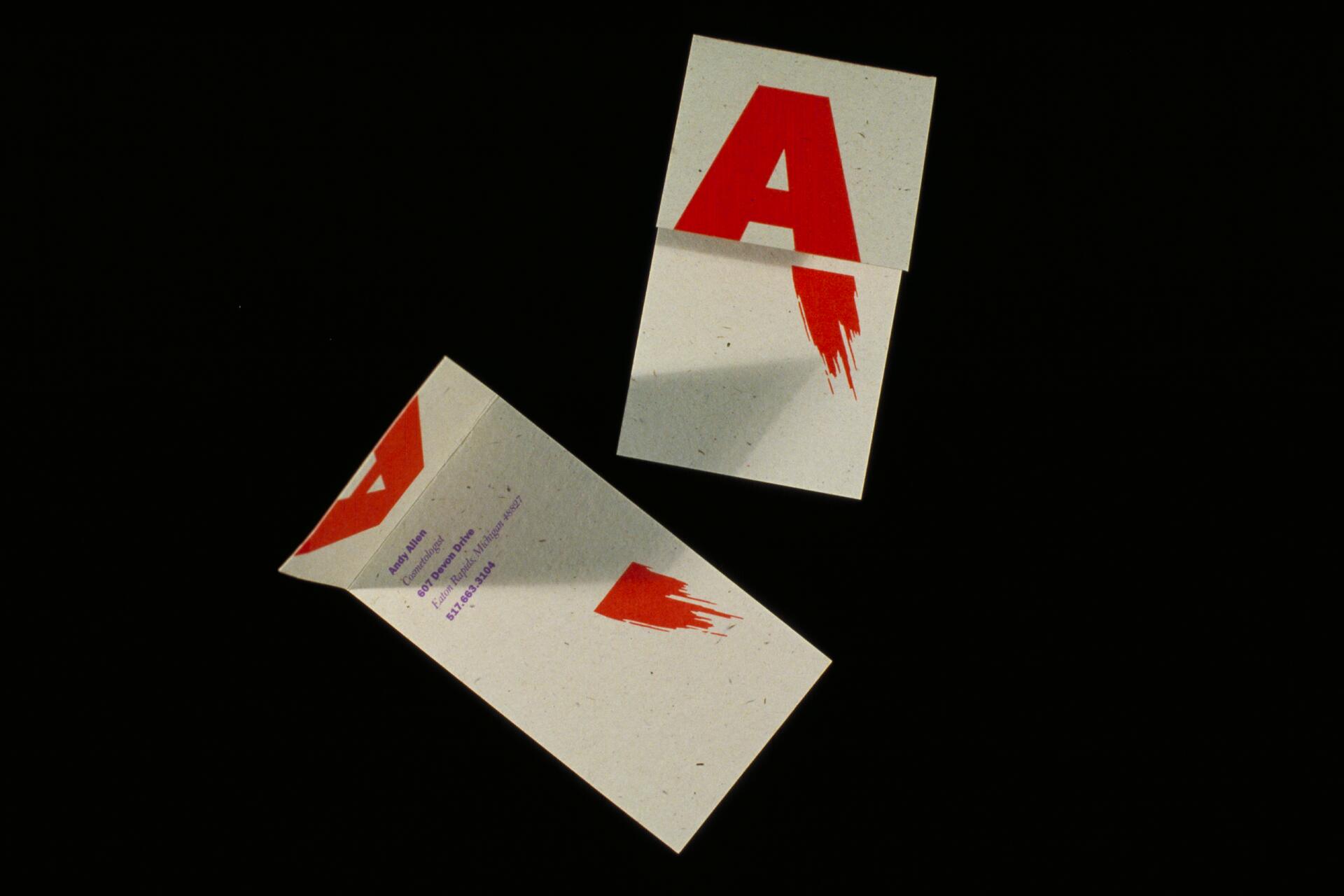 Two business cards with bold red letter "A" design; one closed, the other open with contact details and abstract red brushstroke at the bottom. Black background.