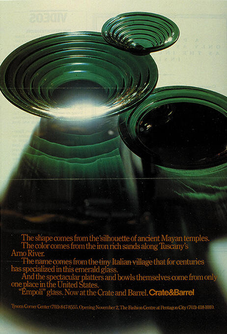 Emerald glass bowls and platters in varying sizes reflect light, with a Mayan temple-inspired silhouette. Text below describes the origin and availability at Crate & Barrel.