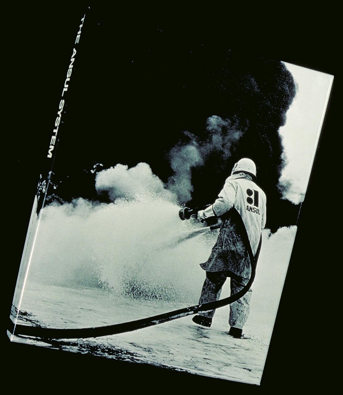 Firefighter spraying foam toward a large billowing cloud of smoke.