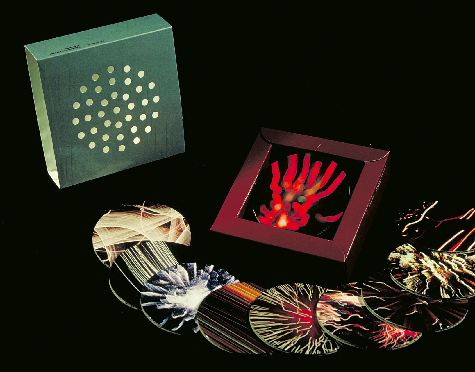 A set of colorful, abstract circular graphics displayed in a row with a red box containing a red-and-orange design resembling a hand. A green box with circular cutouts sits nearby on a black background.