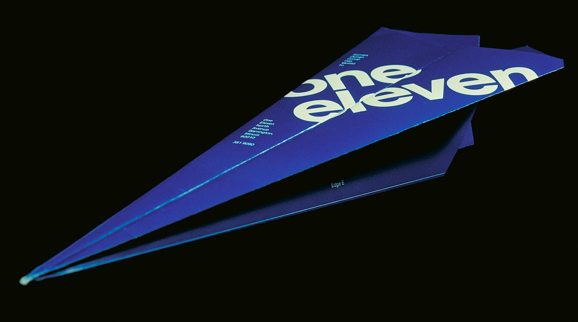 Blue paper airplane on a black background with large white text "one eleven" visible on the wings.