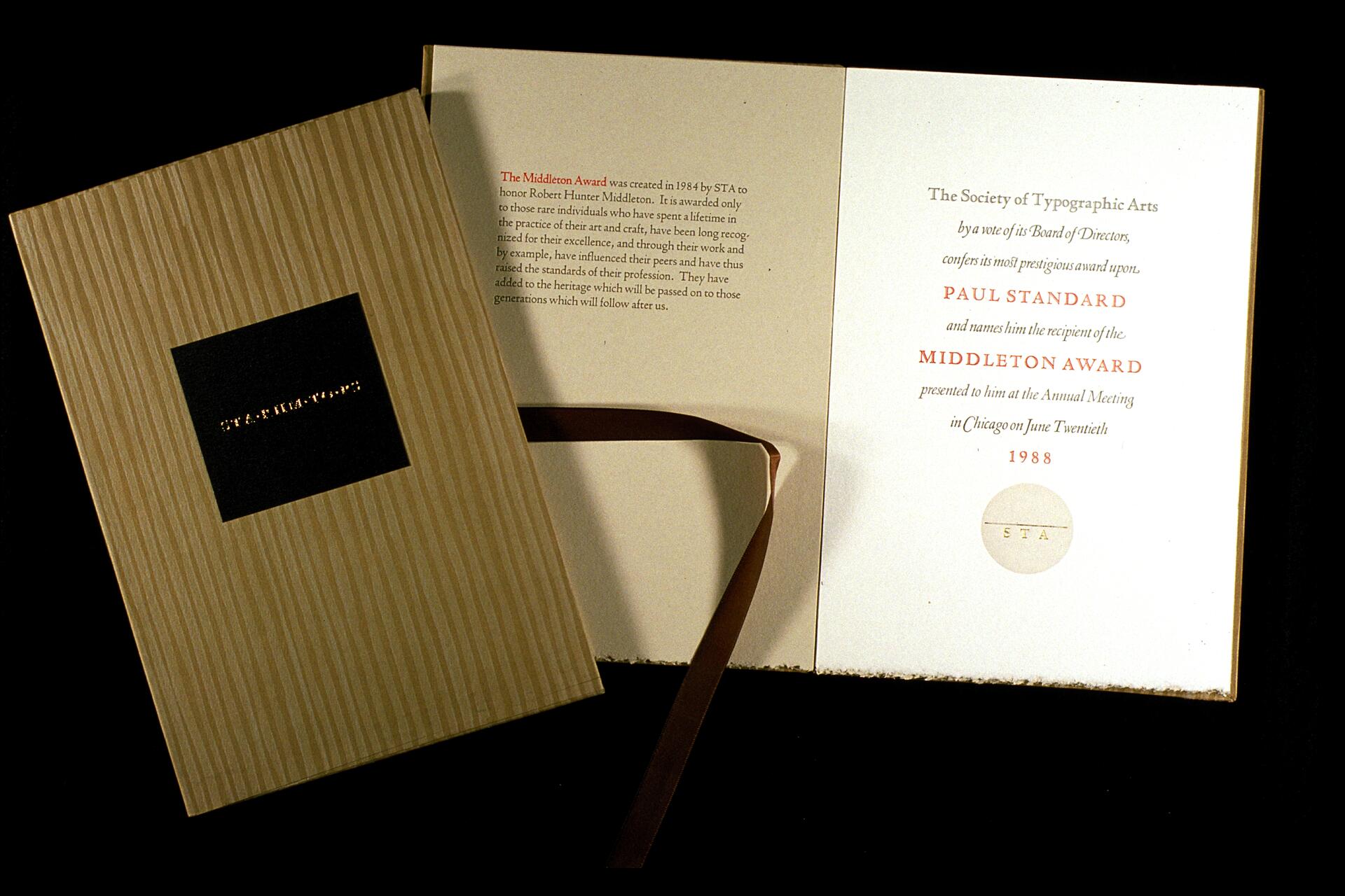 Open award booklet with a beige striped cover and black square label. The inside reveals printed text recognizing Paul Standard as the recipient of the Middleton Award in 1988, with a brown ribbon and minimalist design.